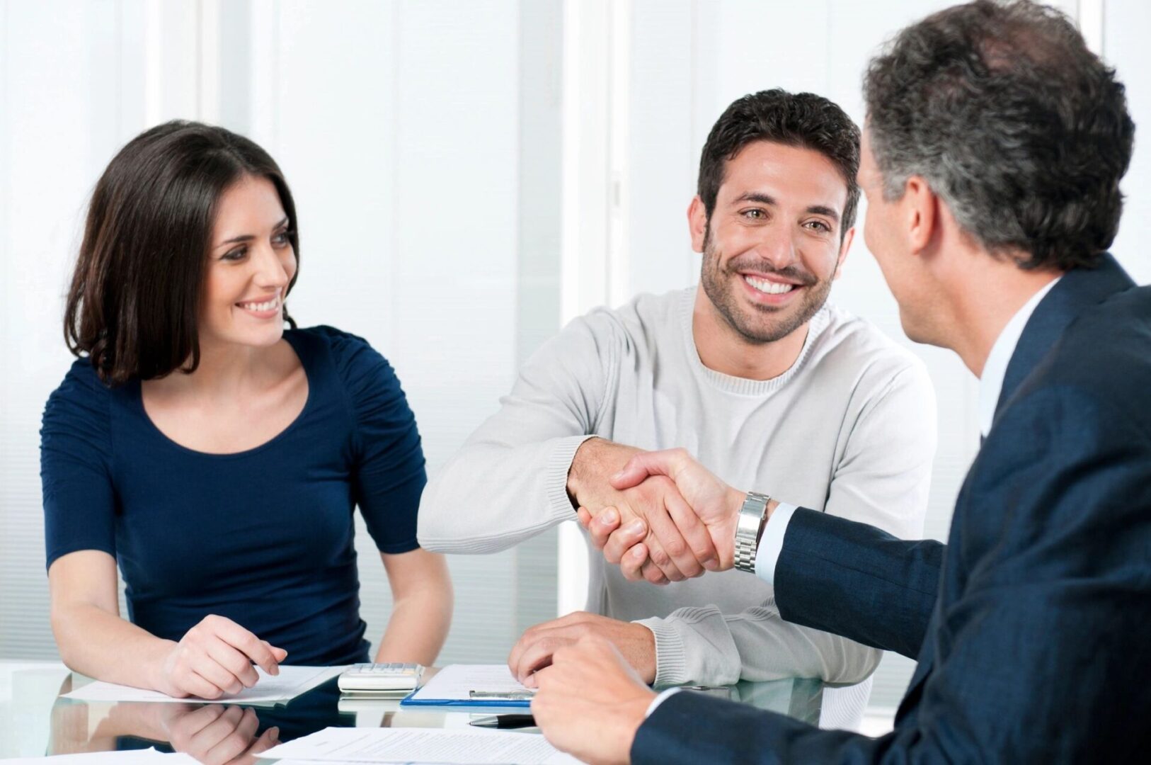 agent shaking hands at table with young couple after helping with income replacement for term life policy